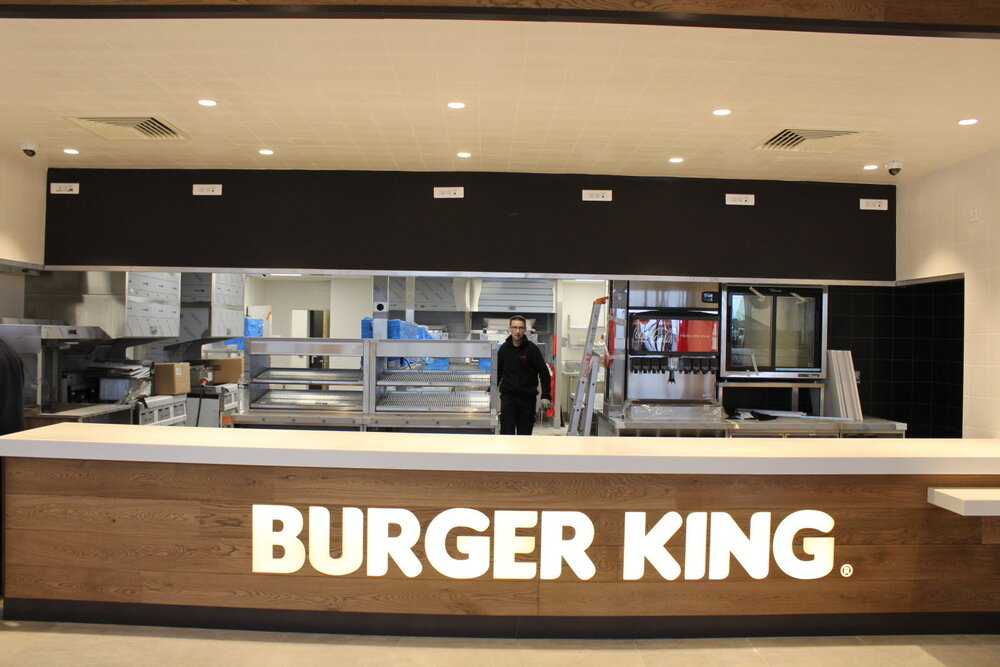 Comptoir Burger King version premium bois clair — totem enseigne, écrans de suivi commande « Collect »