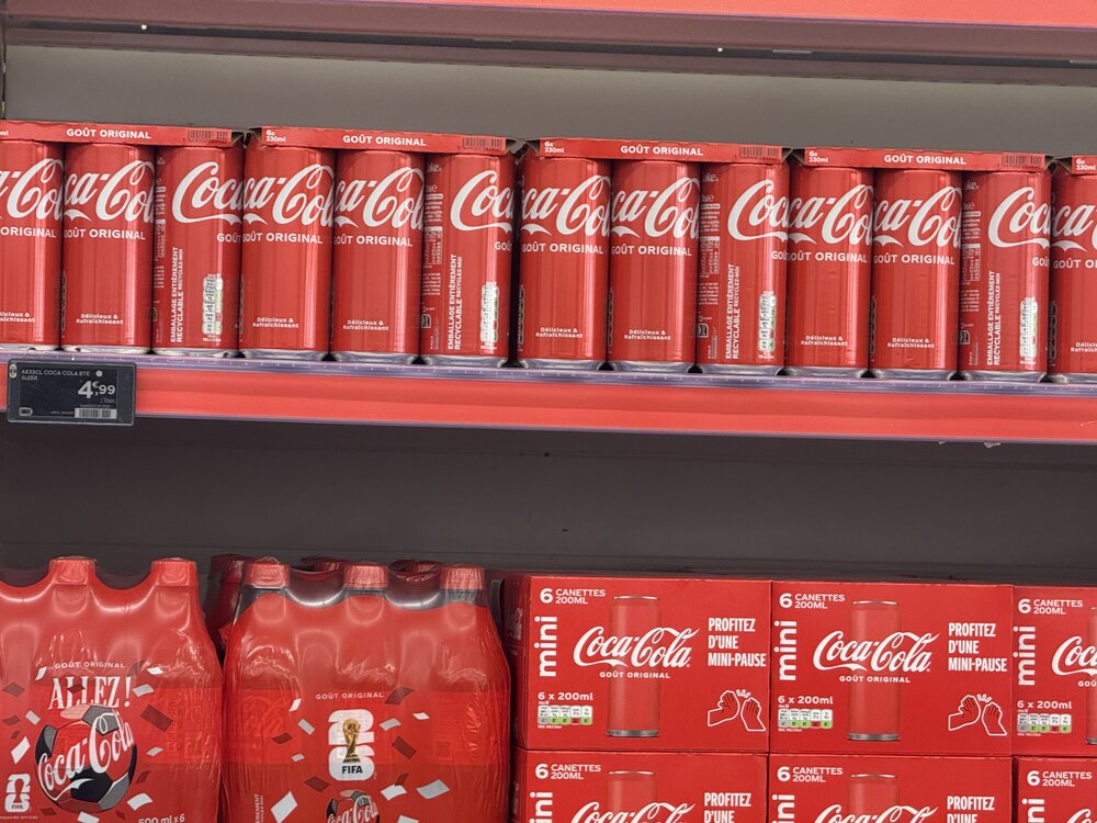Vue large du rayon — Coca-Cola (canettes, bouteilles PET, verre) juxtaposé au rayon jus d'orange