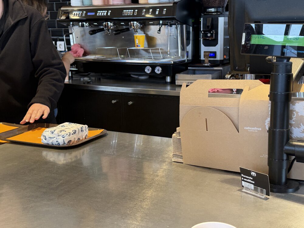 Comptoir Columbus Café — machine expresso, tour de gobelets colorés, boîte à emporter kraft ours