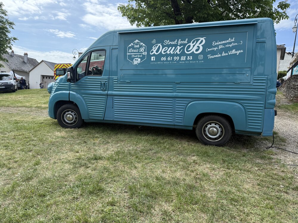 Vue de profil complète du camion — logo Deux B en grand format sur le flanc, réseaux sociaux et tournée des villages