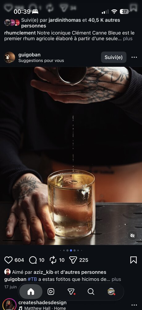 Main tatouée versant des dashes de bitters au-dessus d'un verre à whisky glacé, ambiance de bar sombre