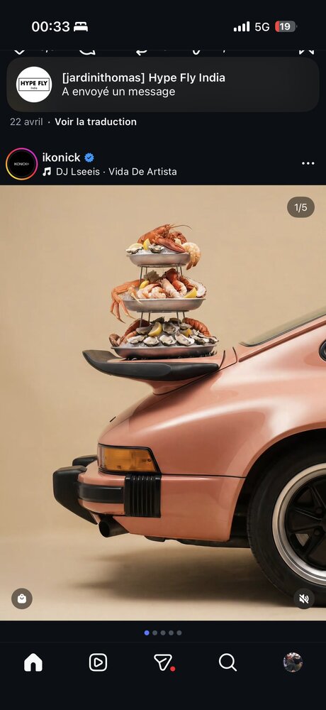 Porsche rose posée sur fond beige, plateau de fruits de mer (crevettes, crabe, huîtres) en équilibre sur l'aileron arrière