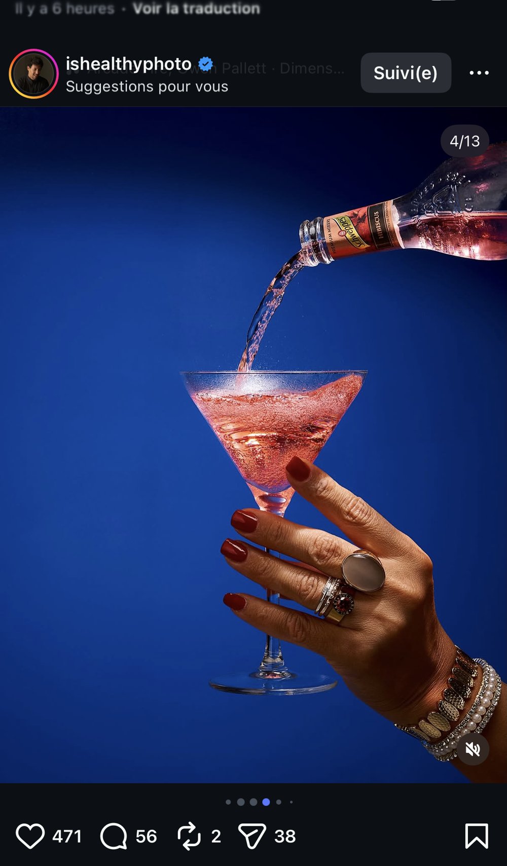 Cocktail rosé versé dans un verre tenu par une main bijoutée, fond bleu nuit