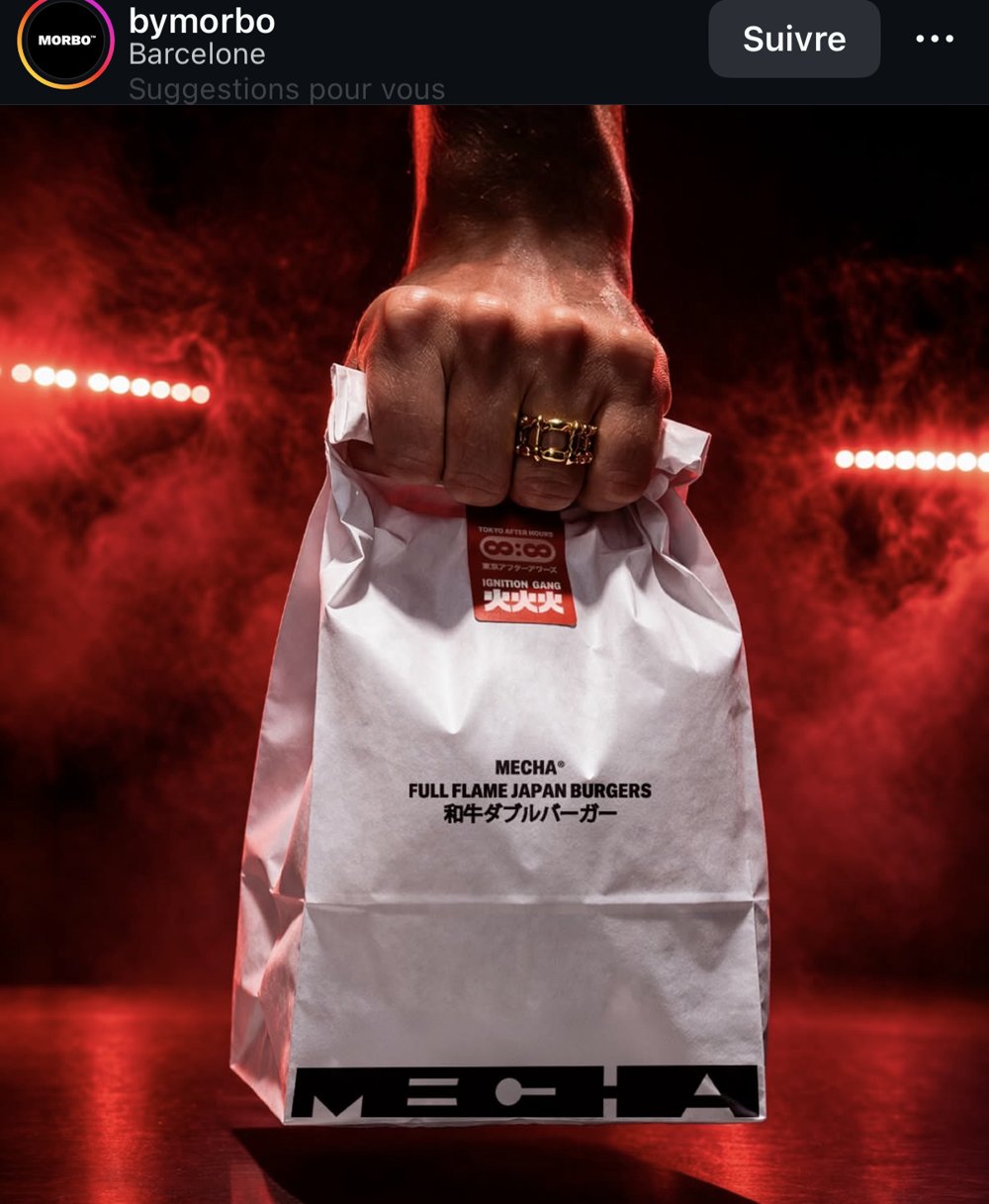 Sac kraft « Mecha — Full Flame Japan Burgers » tenu en main, ambiance néon rouge et fumée