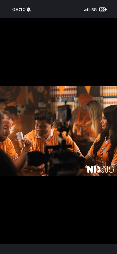 Groupe de supporters en maillots orange autour d'une table, mention « NIX18 » incrustée