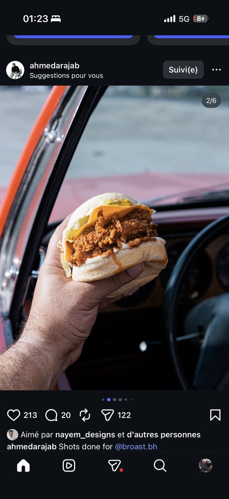 Main tenant un burger poulet croustillant, cadrage serré sur le produit, portière de voiture vintage floutée en fond