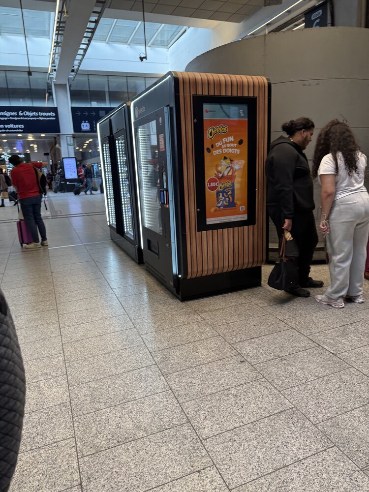 Duo de distributeurs automatiques Selecta en gare — habillage bois clair, écran publicitaire Cheetos
