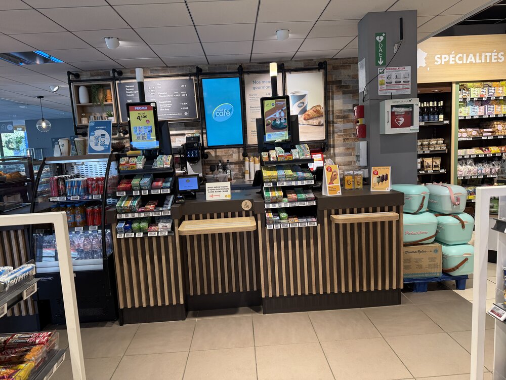 Comptoir intérieur Shell Café — bornes de commande, présentoir snacking, valisettes turquoise en attente de livraison