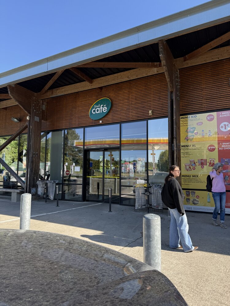 Façade extérieure Shell Café — architecture bois, enseigne ovale « Shell café », bandeau « Shell Select »